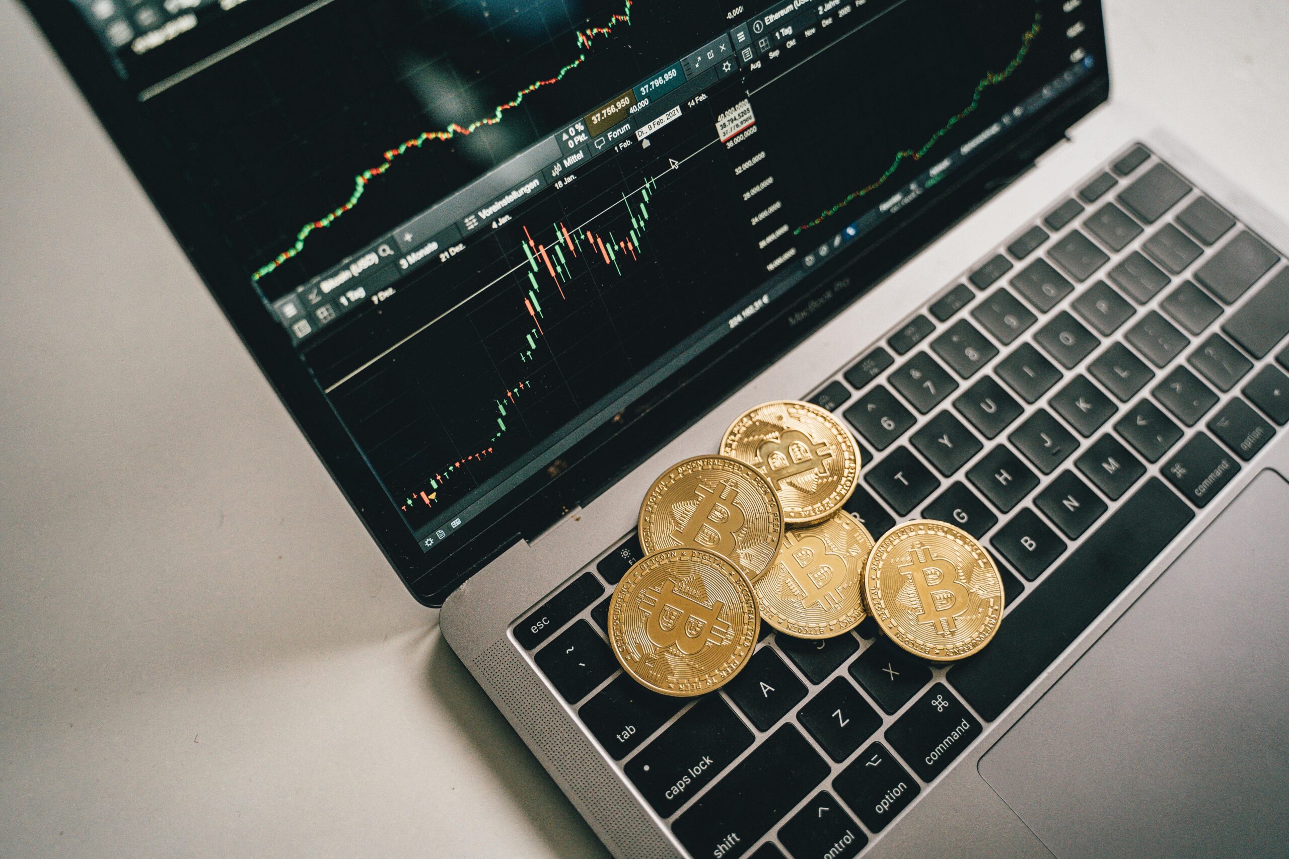 Golden bitcoin coins placed on a laptop keyboard with trading chart displayed on the screen.