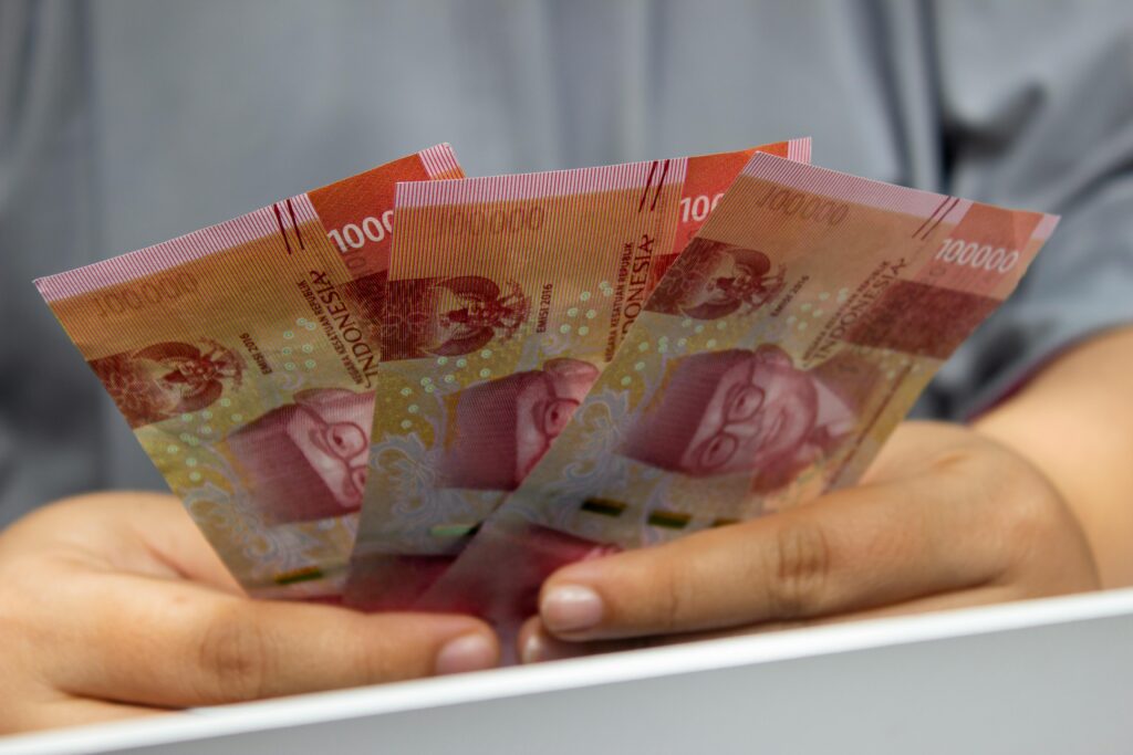 Hands holding multiple Indonesian Rupiah banknotes, showcasing currency details.