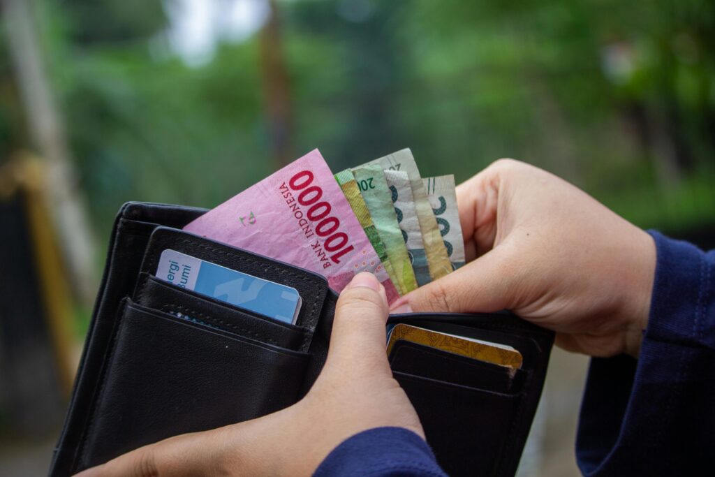 Close-up of hands holding Indonesian rupiah notes in a wallet outdoors.